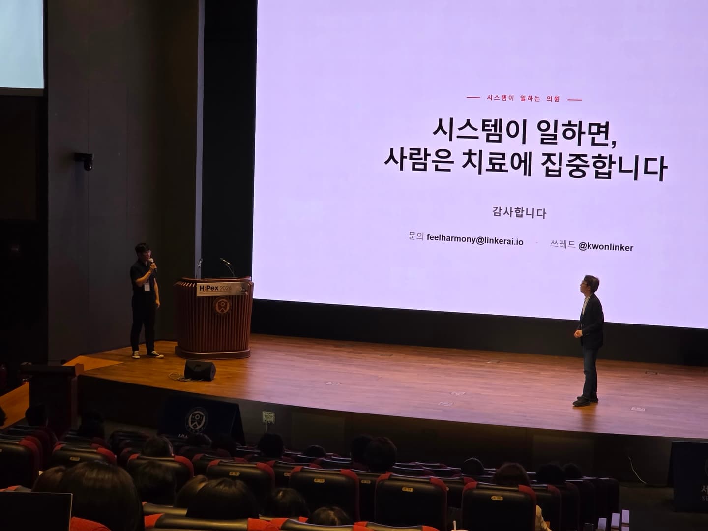 HIPEX 2026 발표 무대와 ‘시스템이 일하면, 사람은 치료에 집중합니다’라는 발표 화면
